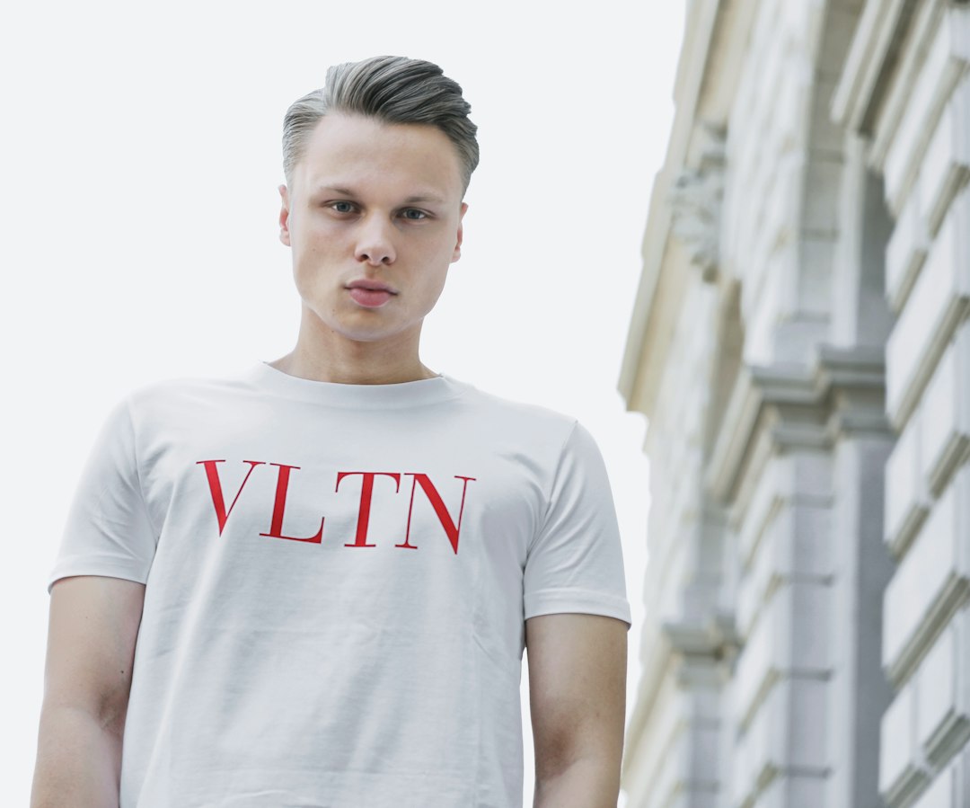A man with styled hair wearing a white t-shirt with red lettering